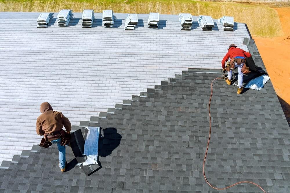 Construction Workers Applying Shingles On Roof