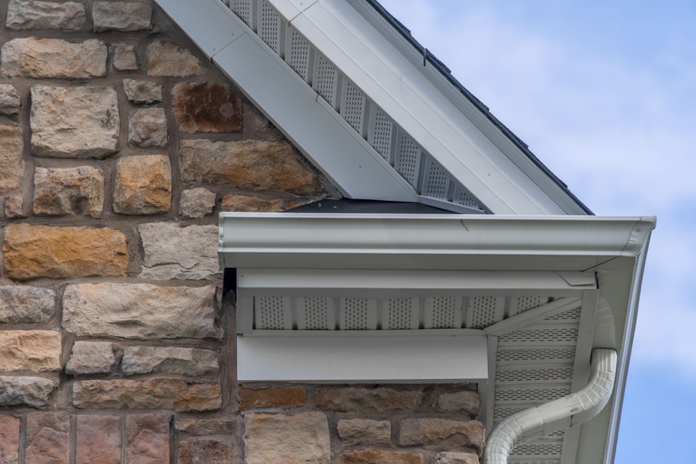 Gable with colored stone siding, white frame gutter guard system, fascia, drip edge, soffit, on a pitched roof attic at a luxury American single family home neighborhood USA