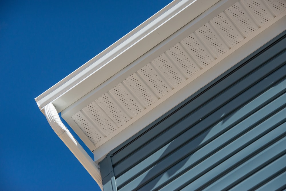 Colonial white gutter guard system, fascia, drip edge, soffit providing ventilation to the attic, with pacific blue vinyl horizontal siding at a luxury American single family home neighborhood USA