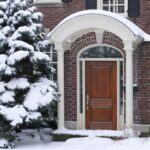 front door of house with snow covered pine tree