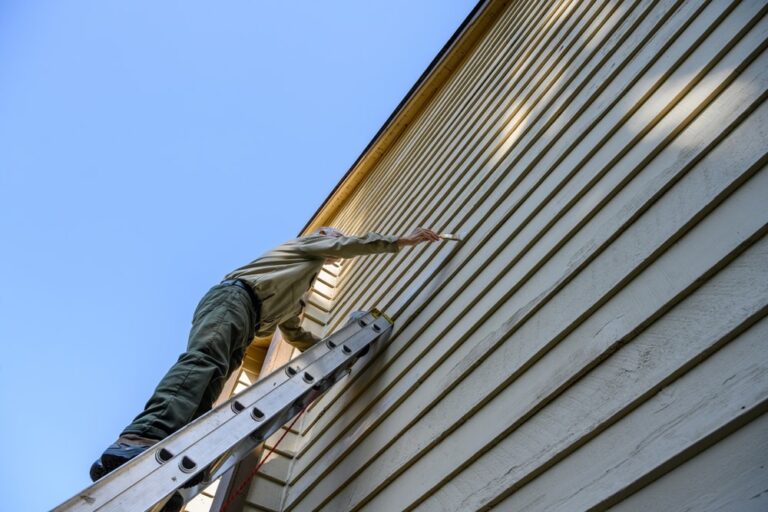 Homeowner on an extension ladder painting sealer on wood siding of the exterior of their house