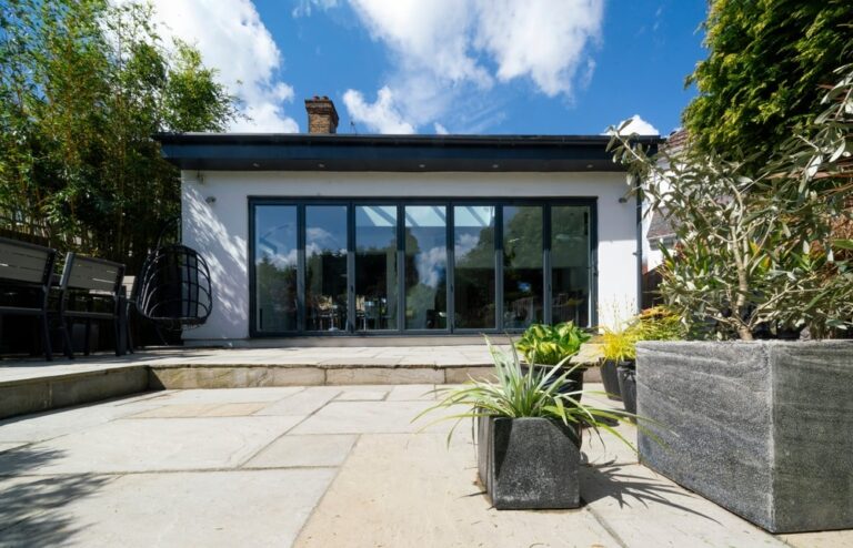 Stylish, closed, bifold doors with plants in summer, spring, with Indian Sandstone patio.