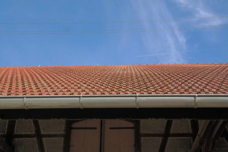 Horizontal view of beige gutter below red roof - Pinnacle Home Improvements