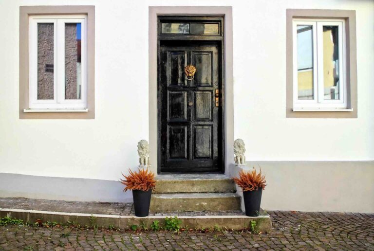 Black door with lion knocker above steps flanked by lion statues & black planters with orange plants - Pinnacle Home Improvements