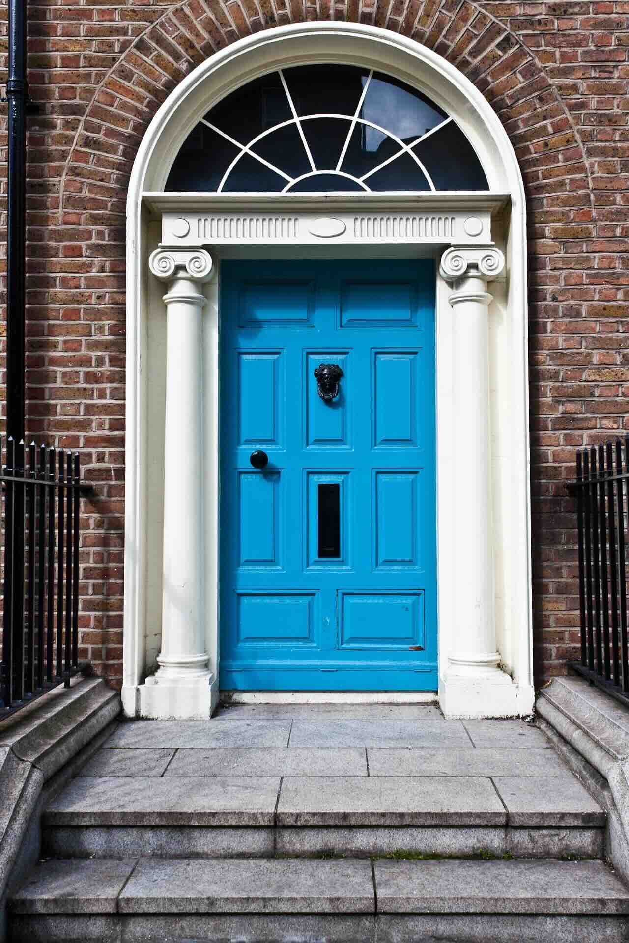 Blue paneled entry door with lion knocker, white columns under arched fanlight, brick facade, & stone steps - Pinnacle Home Improvements