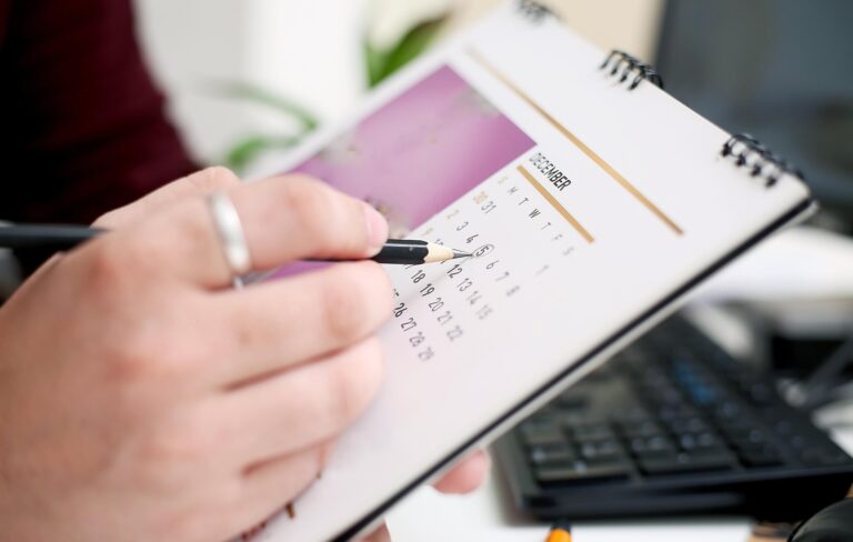 Person's hand marks calendar with pencil, with blurred computer keyboard in background - Pinnacle Home Improvements