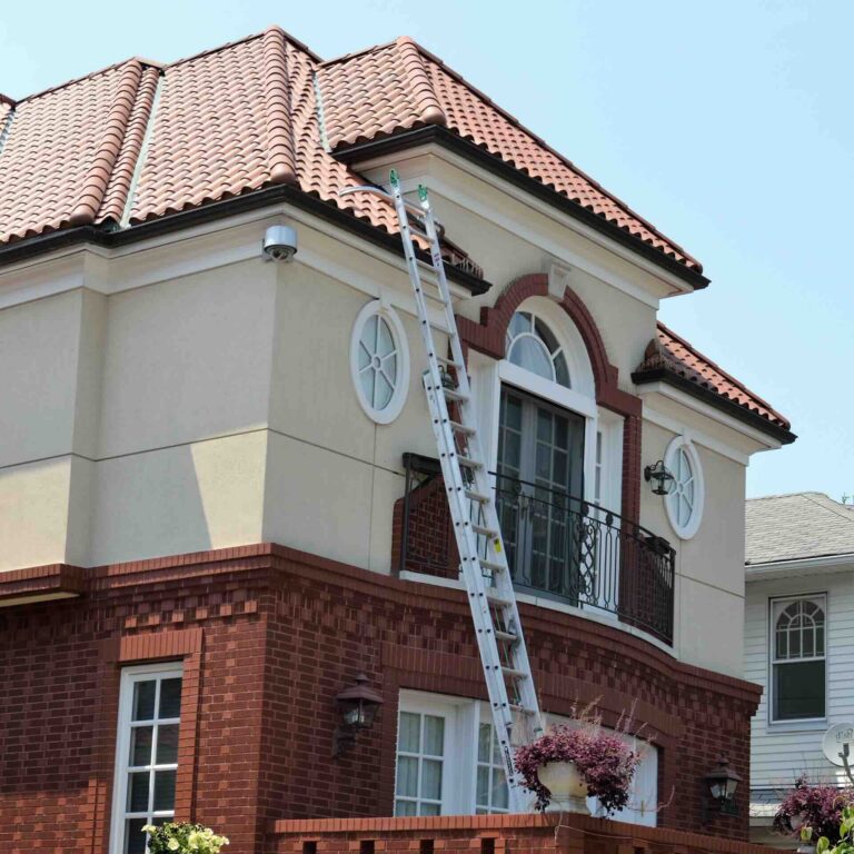 Two-story house exterior with red-tiled roof and ladder leaning against balcony to winterize - Pinnacle Home Improvements