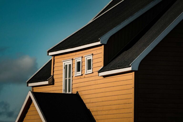 Ochre-colored siding on house with steep dark roof - Pinnacle Home Improvements