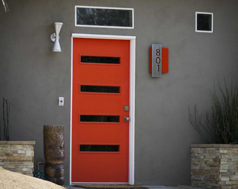 Red modern entry door with 2 horizontal windows, metal street number plaque, and silver sconce in gray wall - Pinnacle Home Improvements