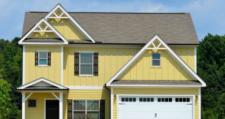 Vertical, yellow siding on 2-story house with white trim, 3 gables, dark shutters, and white double garage door - Pinnacle Home Improvements
